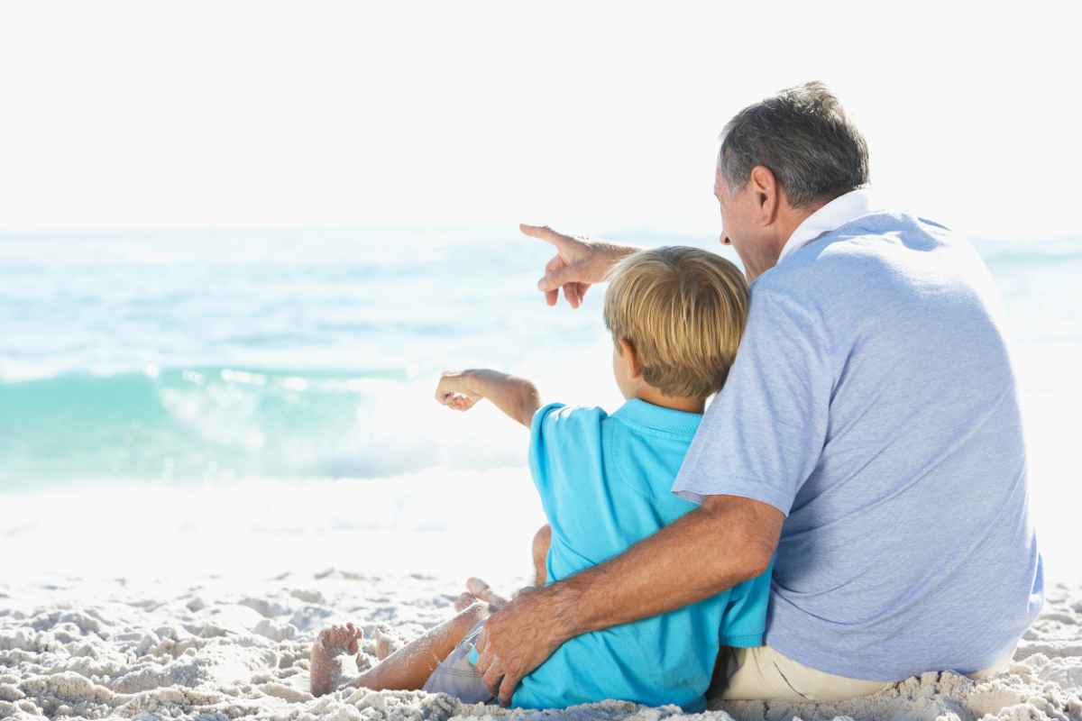 Nonno e nipote seduti in spiaggia ad ammirare il mare