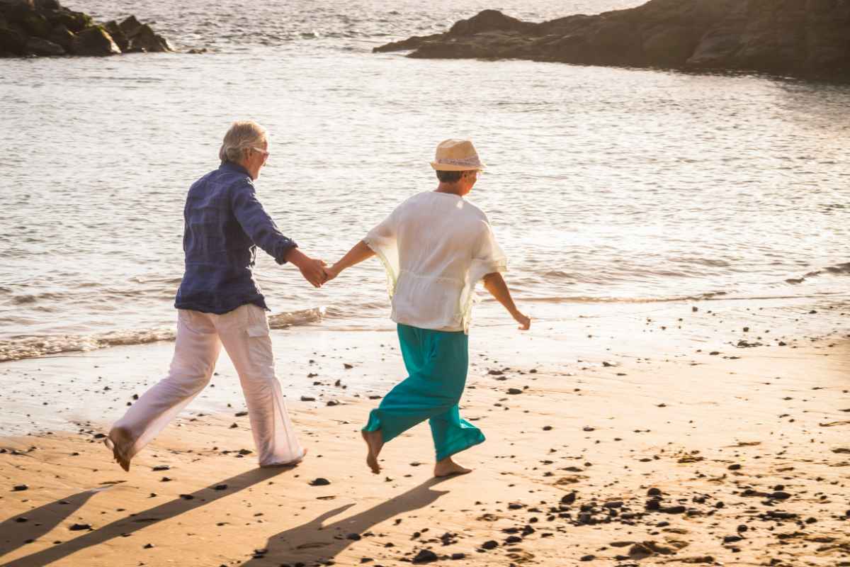 Coppia di anziani che corrono in spiaggia mano nella mano
