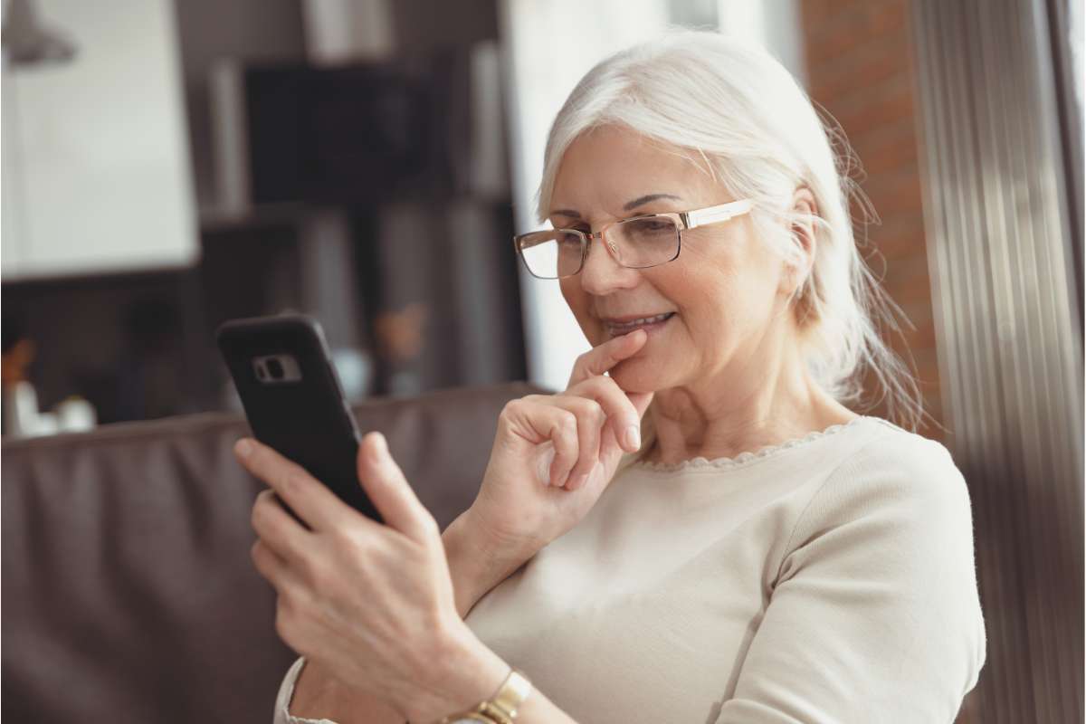 Signora di 60 anni seduta sul divano con in mano lo smartphone